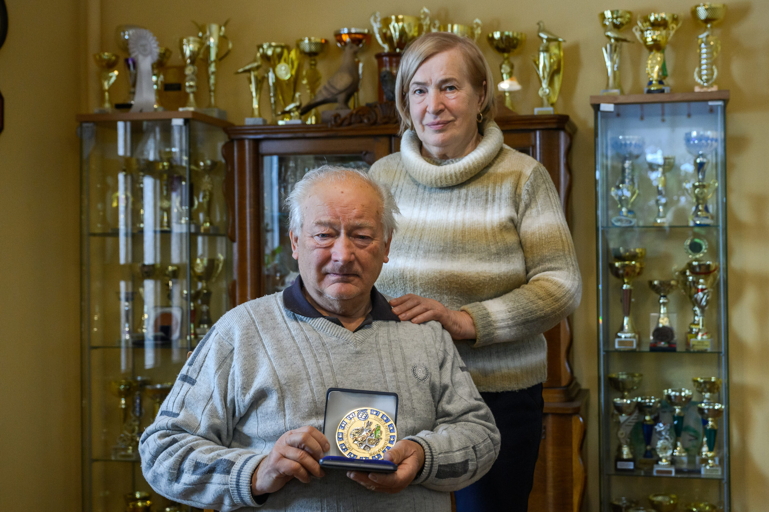 Jaksa János és felesége, Judit a „dicsőségfal” előtt. János bácsi 2009-ben megkapta a kontinens legnagyobb galambtenyésztői díját, az Európa Plakettet, és ugyanekkor Európa mesteri címet is szerzett